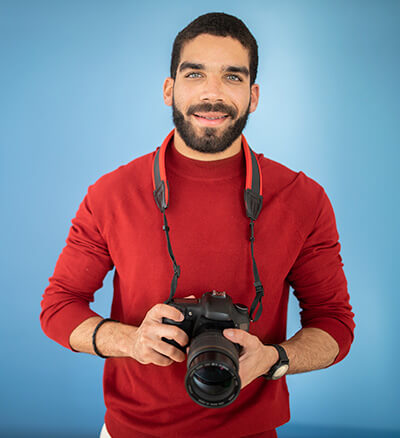 Un hombre de camisa roja sujeta una cámara fotográfica y sonríe